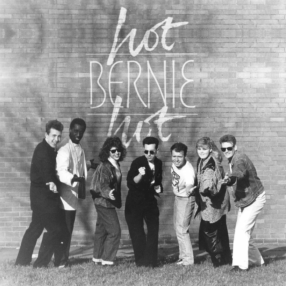 seven piece band pose in front of a wall with Bernie Hot Hot written on it.